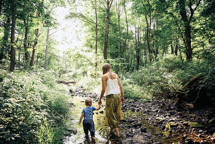 A mother and child walking through a forest creek