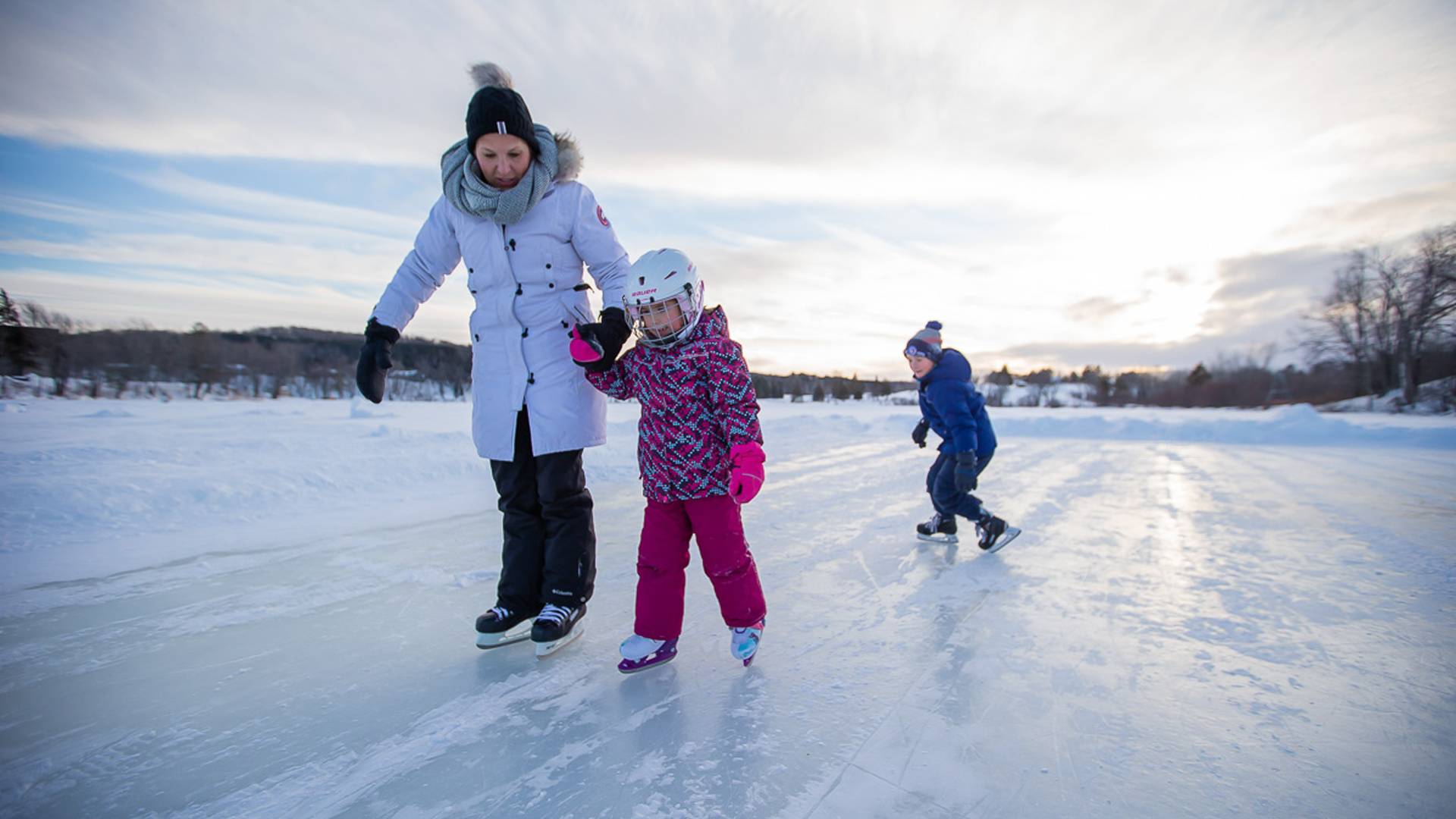 A woman and two children skating on a lake at Deerhurst Resort